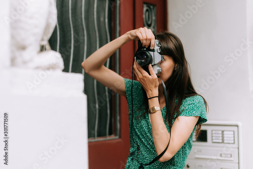 elegant woman wearing a green dress is taking a picture with an old film camera