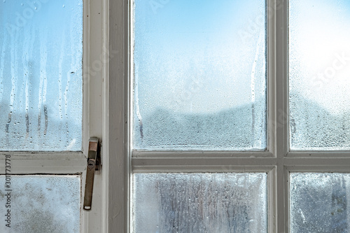 Cold room interior looking out onto water condensation formed on interior windows during early winter. Showing the wooden frame and metal lock, the condensation is known to cause damp and mould. photo