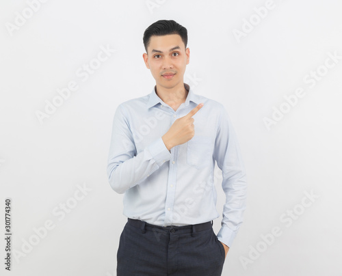 Young asian business man with blue shirt pointing to the side with a finger to present a product or an idea while looking to camera isolated on white background.