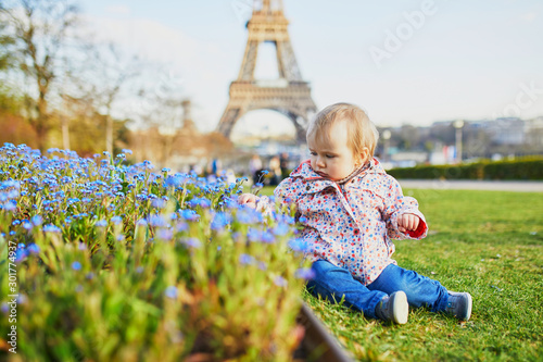 One year old girl sitting on the grass with blue flowers and Eiffel tower © Ekaterina Pokrovsky