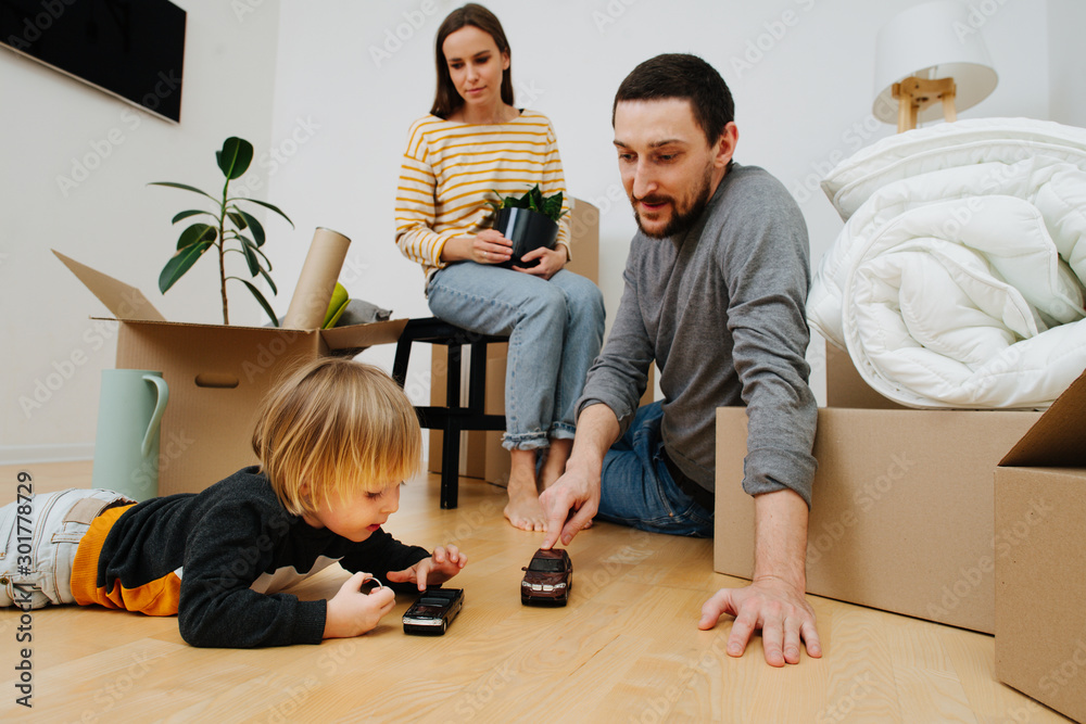 Happy young family moving to a new home, playing with kids toys while unpacking