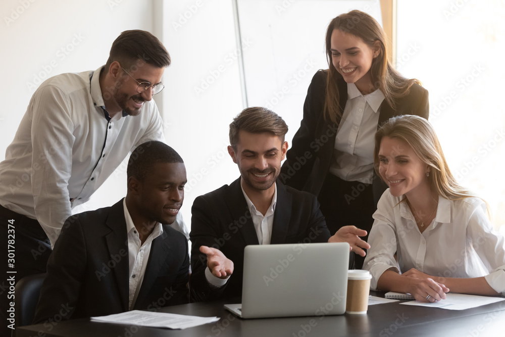 Smiling diverse employees cooperating in office using laptop