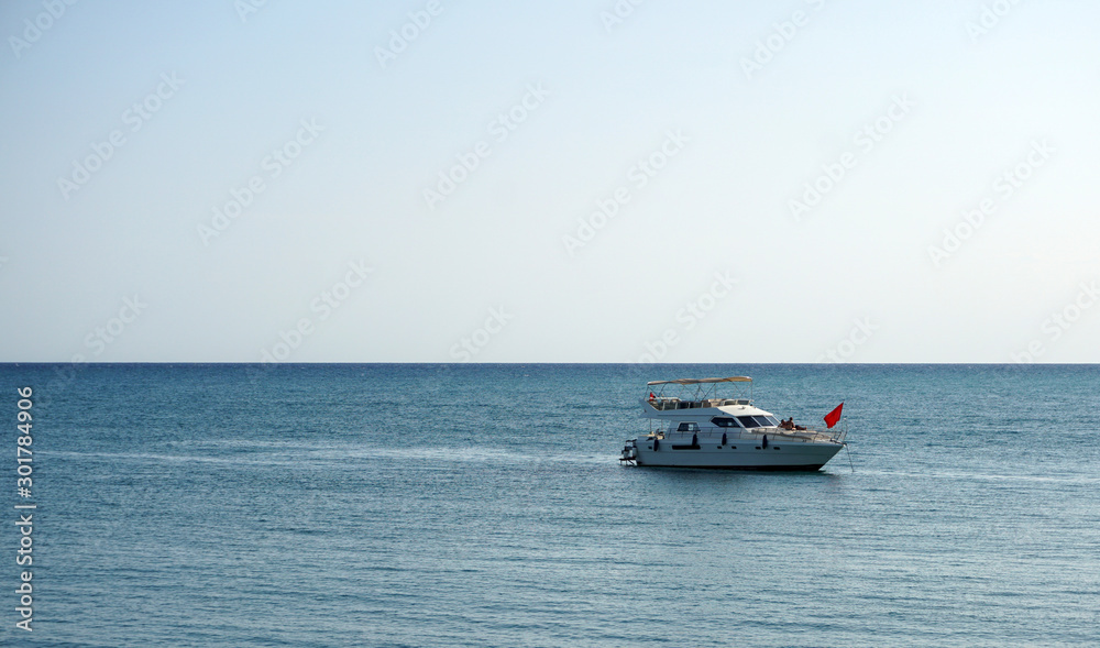 White motor boat with a red flag on the background of the sea and horizon. A wonderful trip by sea on a yacht. Unforgettable summer vacation at sea.
