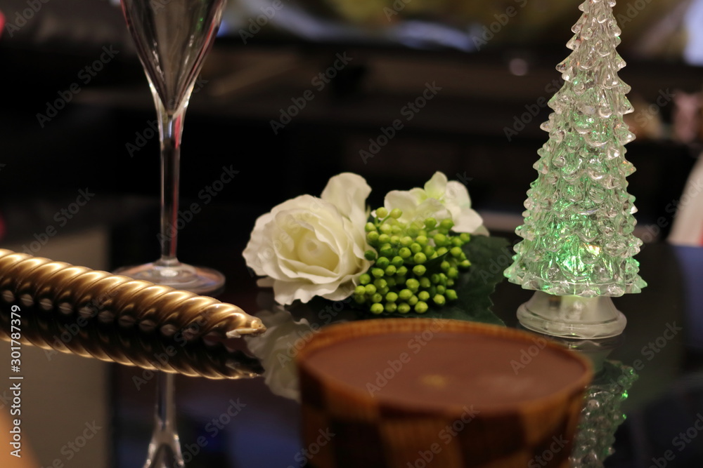 テーブルの上のケーキとクリスマスツリーとグラスとろうそくと白い薔薇	