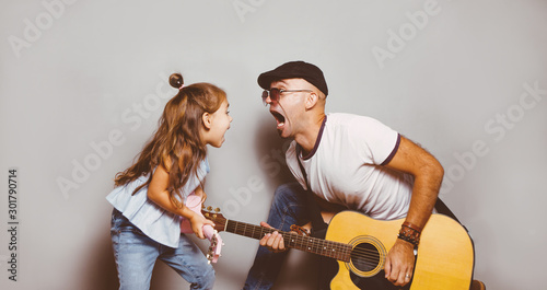 Beautiful little girl playing guitar with her father. Funny lifestyle picture. Happy family timespending. Girl holding pink ukulele ang singing and jumping, photo