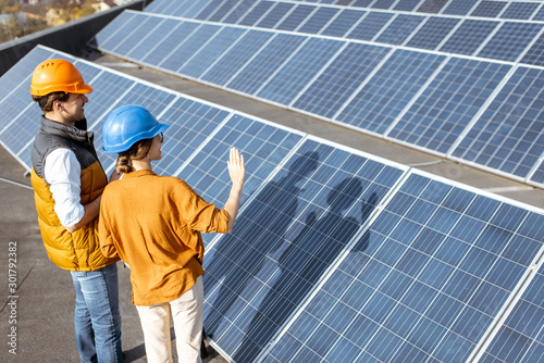 Two engineers or architects examining the construction of a solar power plant, standing with digital tablet between rows of solar panels