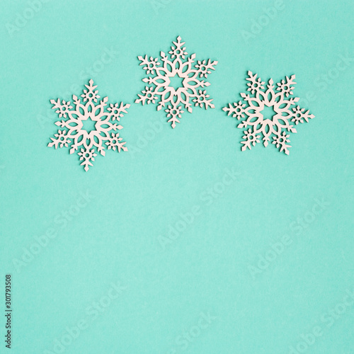 Christmas greeting card with wooden snowflakes on mint paper background with copy space. New Year decoration. Creative minimal winter celebration concept.