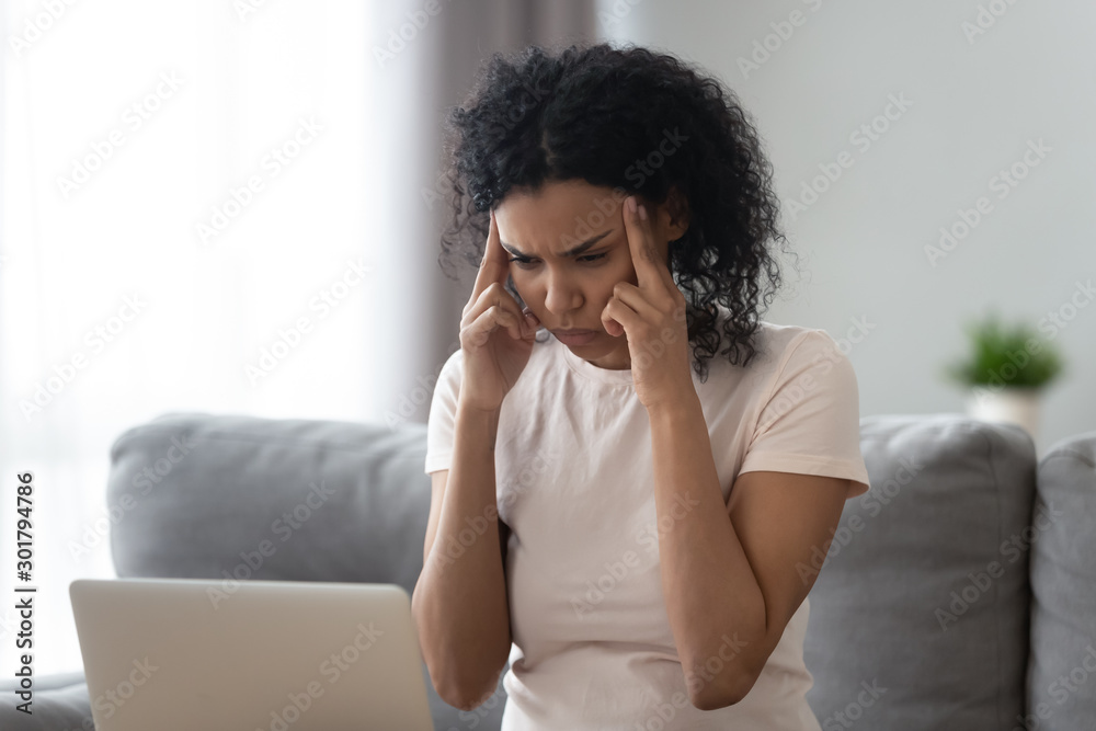 Exhausted African American woman massaging temples, using laptop Exhausted African American woman massaging temples, using laptop