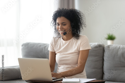 Smiling African American woman in headset using laptop at home