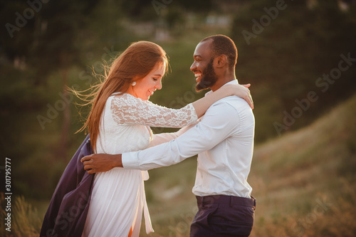 mixed couple of people hugging on sunset background