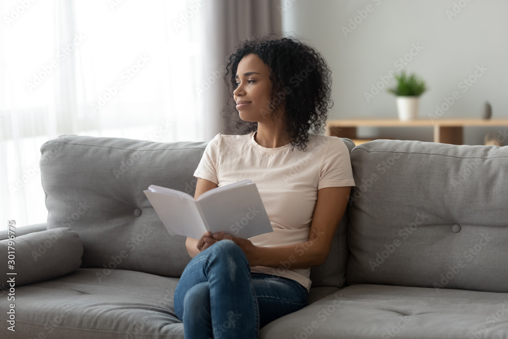 Calm satisfied African American woman relaxing at home, holding book Calm satisfied African American woman relaxing at home, holding book