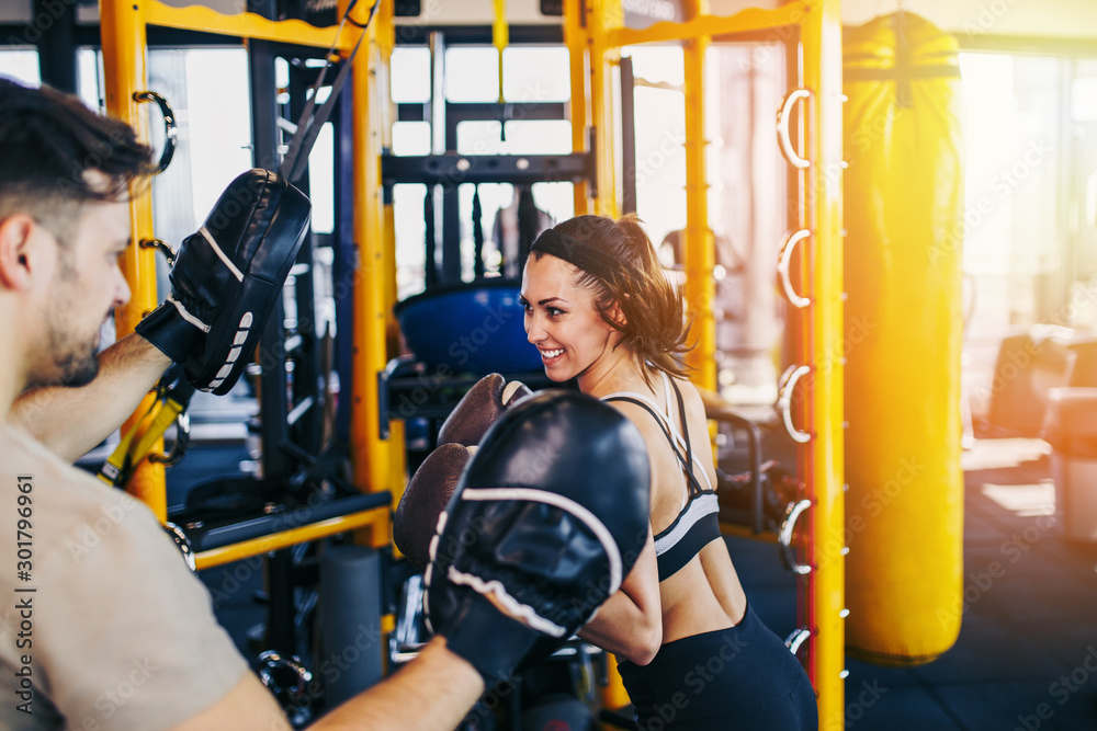 Obraz premium Young attractive woman with instructor on kickboxing training. She hitting or punching in big yellow boxing bag.
