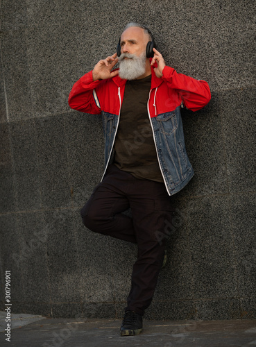 A trendy bearded senior man listening to music outdoor. Fashion mature man. © lashkhidzetim