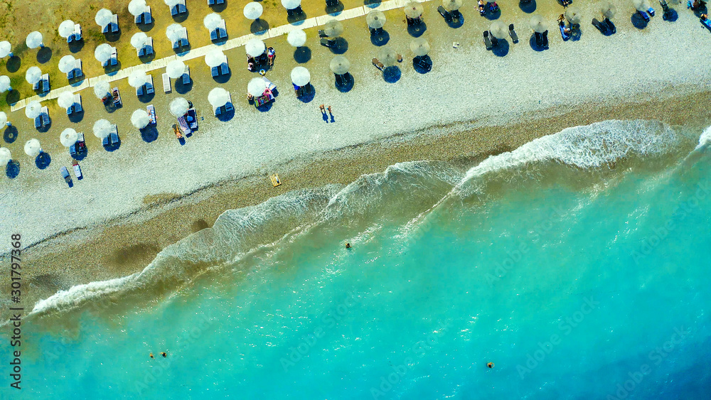 Aerial view of amazing turquoise sea with brown straw umbrellas and sun loungers. Beautiful sunny summer day in Greece, Mediterranean sea