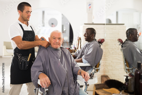 Barber putting on hairdresser cloak to elderly male client