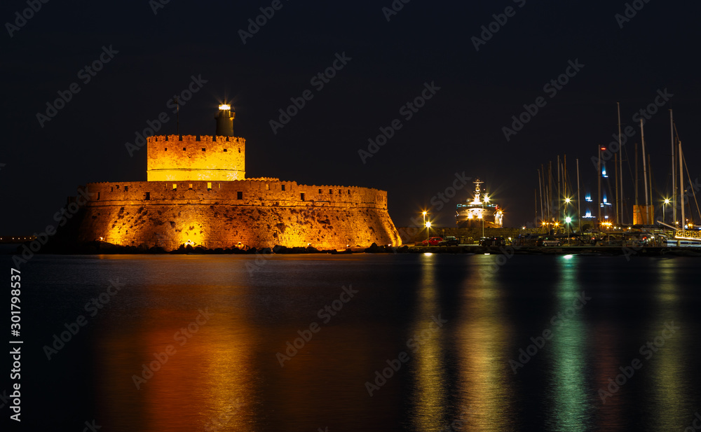 night Marina port Mandraki Rhodes island with a large yacht at the pier on background of the ancient fortification, the middle ages.