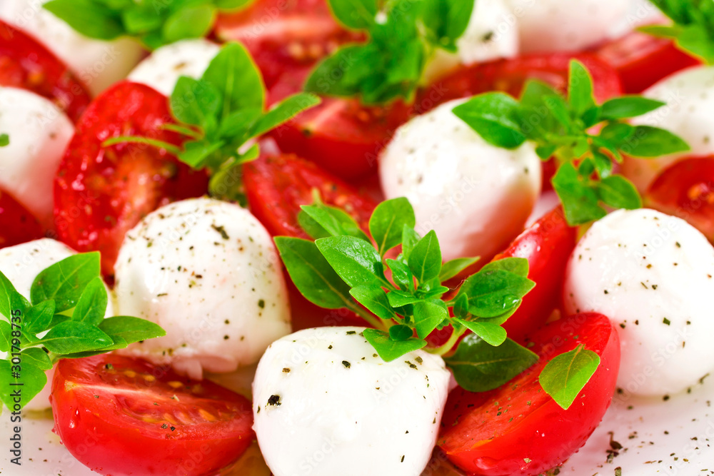 Caprese salad background. Ripe red cherry tomatoes, white mozzarella cheese balls with young basil green leaves and spices. Caprese salad background. Ripe red cherry tomatoes, white mozzarella cheese balls with young basil green leaves and spices.