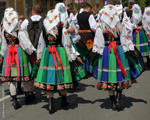 Local Polish people in traditional folk costumes from Lowicz region walk on street celebrating Corpus Christi holiday