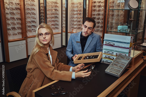 Woman is choosing her new glasses at optical store with help of shop consultant.