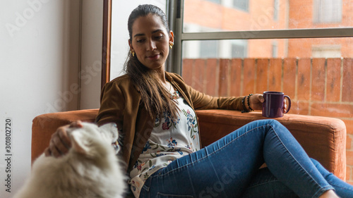 Beautiful latin woman resting while drinking a beverage with her pet