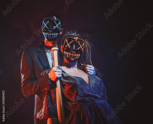 Crazy couple in spooky masks are posing for photographer with baseball bat.