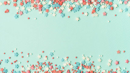 Festive border frame of colorful pastel sprinkles on blue background with copy space in center. Sugar sprinkle dots and stars, decoration for cake and bakery. Top view or flat lay. Banner