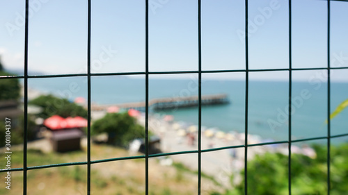 in the foreground is a fence, and in the background is a sea, pier and beach. Vacation and outdoor activities concept © Jimmy Tudeschi
