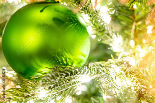 Shiny Christmas green ball hanging on pine branches with festive background