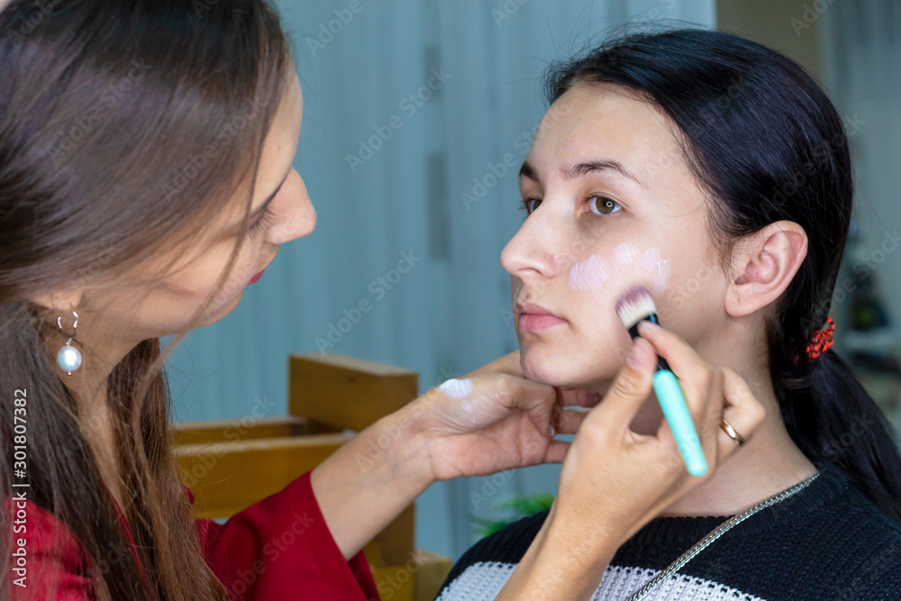 Close-up portrait of woman applying cosmetic Foundation on face using makeup brush. Makeup artist stylist doing makeup Close-up portrait of woman applying cosmetic Foundation on face using makeup brush. Makeup artist stylist doing makeup