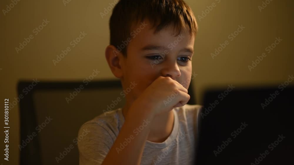Little boy looking at the notebook display in the night. Child use laptop and watching video