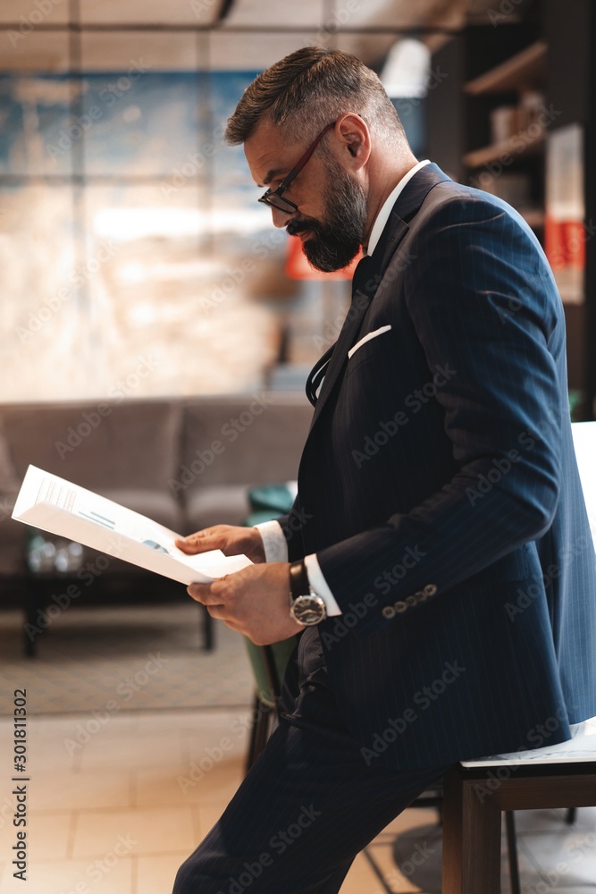 Fototapeta premium Stylish businessman standing near table in the office and reading documents