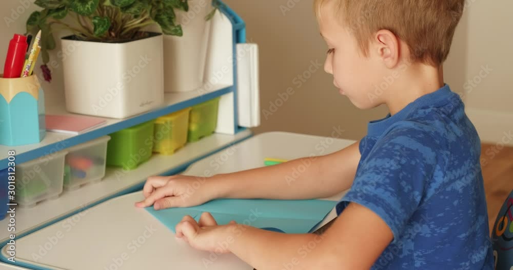 Boy of 8 years makes an airplane out of paper and launches it. The child's leisure time at home. A clever boy designs an airplane. Caucasian boy does the toys from paper. Real time.