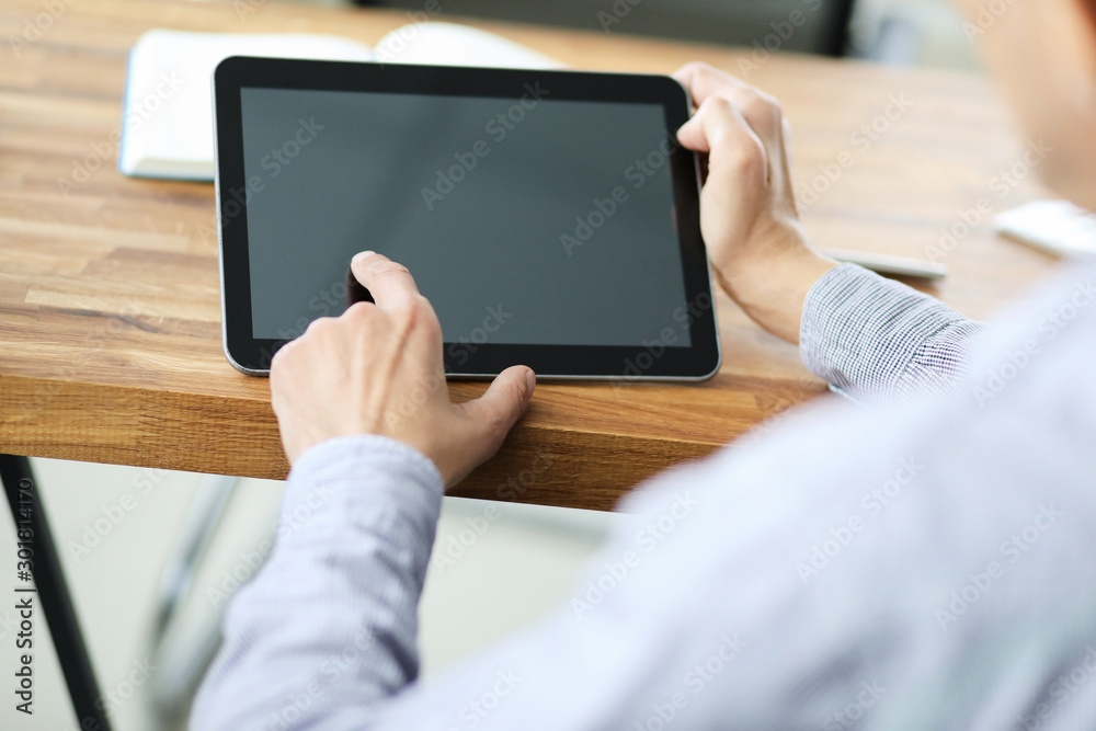 Man's hands holding blank tablet device over a wooden work space table.