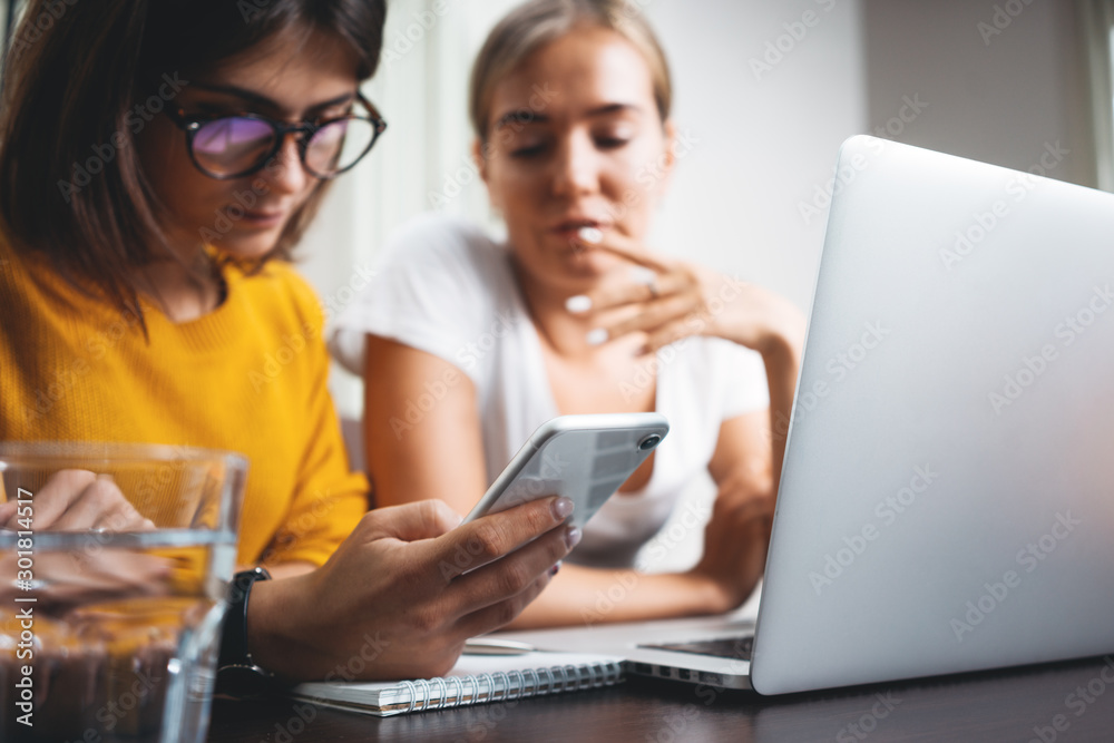 Group of happy woman working together and using digital gadgets at open space. Close-up of female hands hold modern smartphone at her workplace at office Group of happy woman working together and using digital gadgets at open space. Close-up of female hands hold modern smartphone at her workplace at office