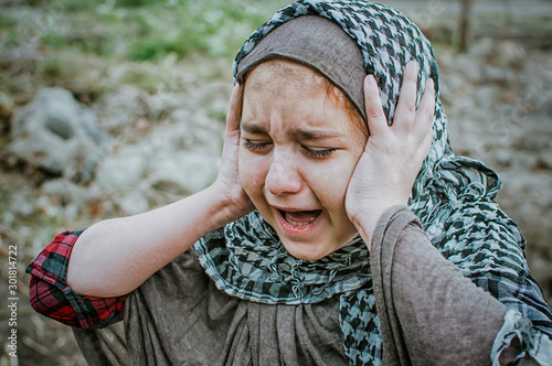 a refugee child in the war, a Muslim girl with a dirty face on the ruins, the concept of peace and war, the child is crying and waiting for help.