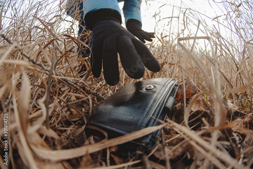 Lost wallet in a grass on the ground and female hand picking up it from a ground. Close up. Fisheye view.