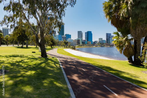 Trees and grass on the shores of the Swan River in Perth, Western Australia, with a cycle path heading to the city centre and its iconic skyscrapers