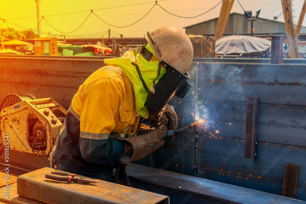 The welder is welding a roof truss of steel structure work with process Flux Cored Arc Welding (FCAW) and dressed properly with personal protective equipment(PPE) for safety, at industrial factory. The welder is welding a roof truss of steel structure work with process Flux Cored Arc Welding (FCAW) and dressed properly with personal protective equipment(PPE) for safety, at industrial factory.