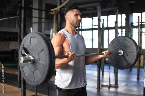 Muscular man working out in gym doing exercises with barbell at biceps.