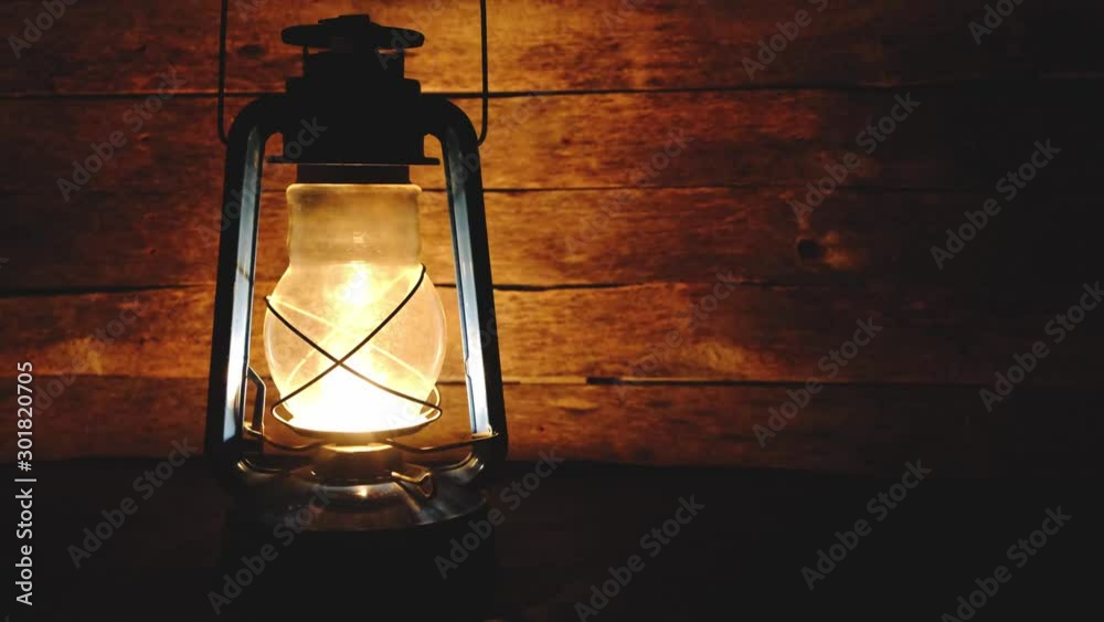Kerosene lamp burns in the dark, sways in the draft and illuminates a wooden background of boards.