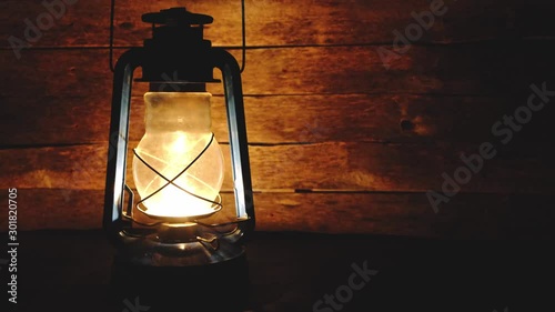 Kerosene lamp burns in the dark, sways in the draft and illuminates a wooden background of boards. photo