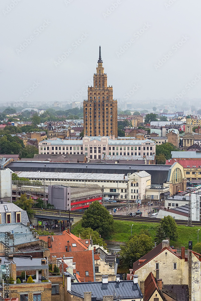 Obraz premium Aerial view of Latvian Academy of Sciences, Riga Central Market, Bus station and Riga Old Town from Saint Peter church on foggy and rainy day, Riga, Latvia. Stalin-era skyscraper. Soft focus