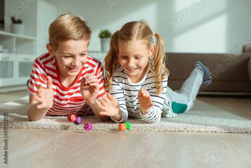 Fototapeta Portrait of two cheerful children laying on the floor and playing with colorful