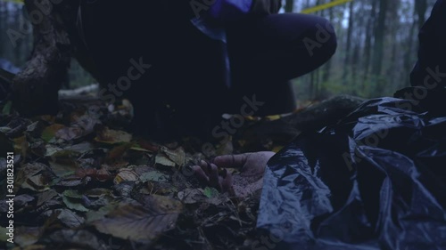 Hand of murder victim on ground in forest, investigator collecting evidence