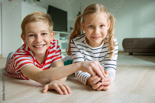 Portrait of two cheerful children laying on the floor and playing with colorful dices