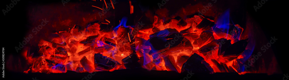 Fototapeta premium Hot wooden coals in the dark. Grill with hot coals and beautiful magic sparks with blue flame