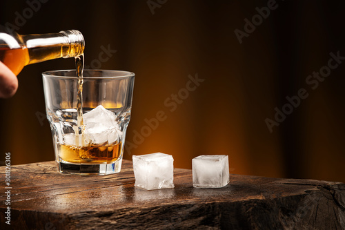 Pouring whiskey into a glass with ice. A glass of alcoholic beverage on a wooden table.