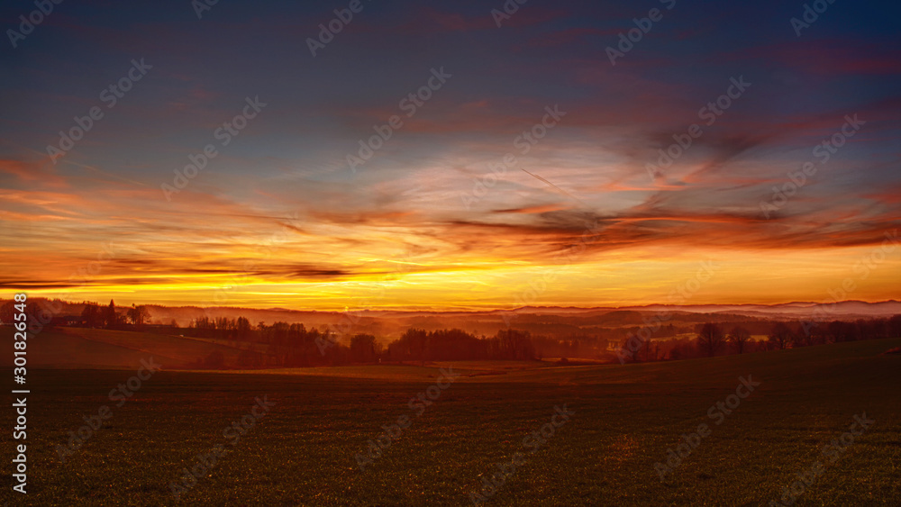 sunset over landscape - field in the foreground, red and yellow clouds in the sky