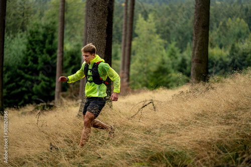 Fototapeta Naklejka Na Ścianę i Meble -  A young athlete in barefoot shoes runs down the mountain. Mountain run. Cross Country Running. Individual sports