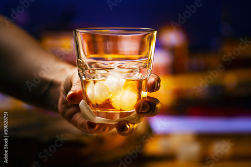 A glass of alcoholic beverage in hand. Whiskey cocktail with ice